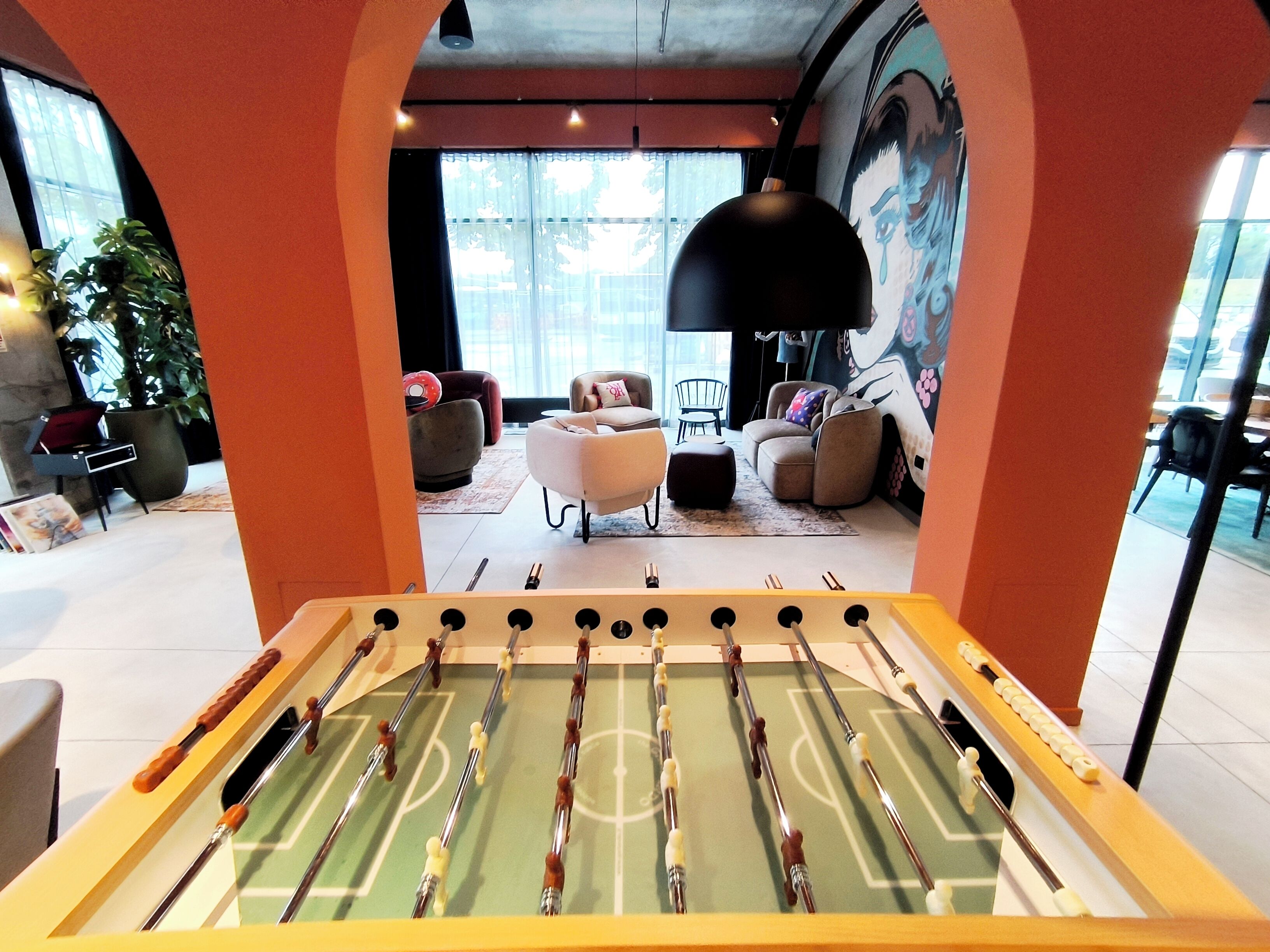 Een tafelvoetbaltafel in een moderne lounge met een groot raam, comfortabele zithoek en een muurschildering.
