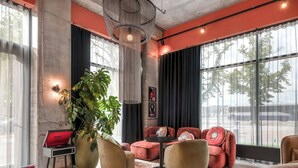 A modern living room with a large window, a potted plant, and a red sofa. - Moxy Verona (Verona)