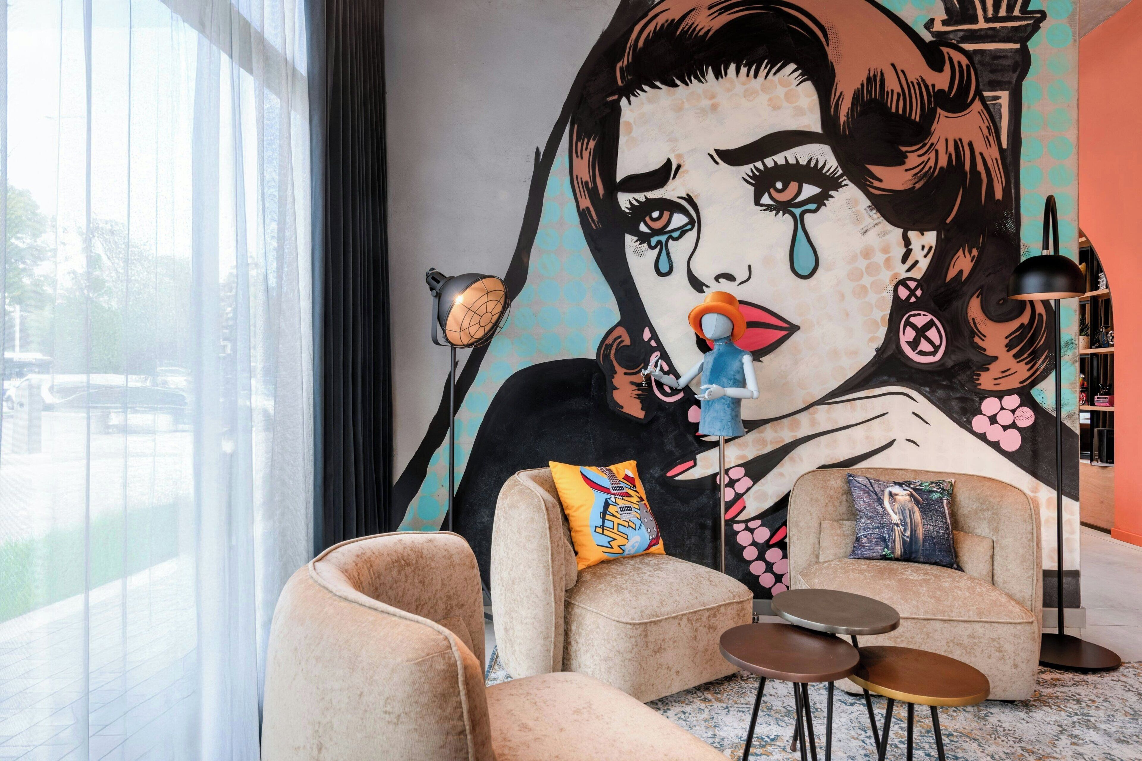 A modern living room with a large mural, comfortable seating, and a view through large windows.