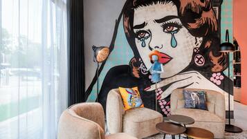 A modern living room with a large mural, comfortable seating, and a view through large windows.