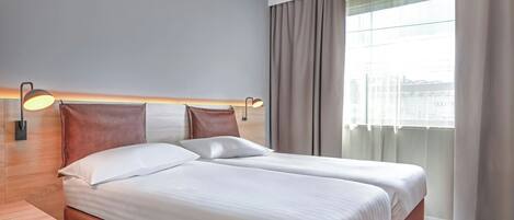A hotel room with two beds, a nightstand, and a window with curtains.