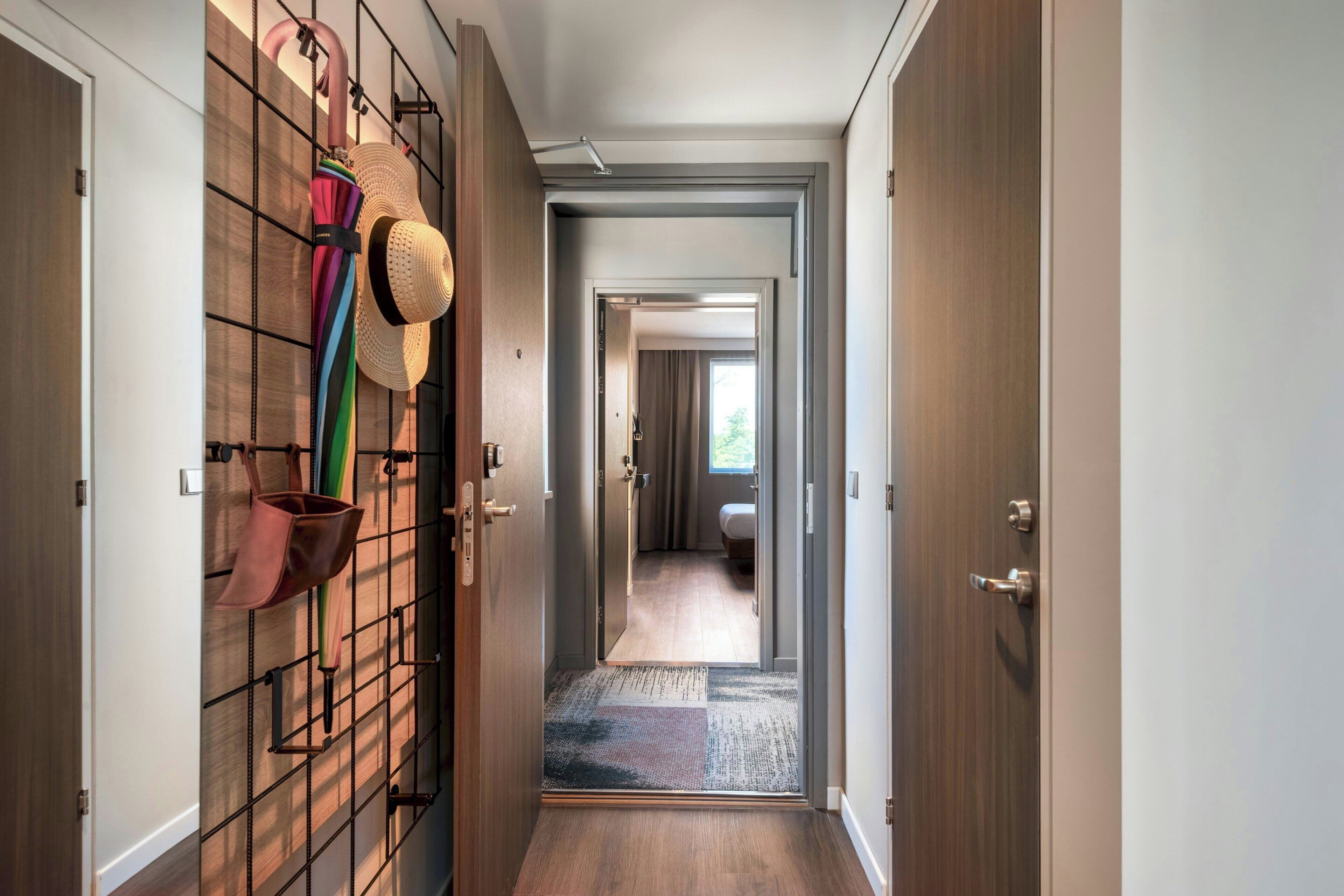 A hallway with a wooden floor, a patterned rug, and a wall-mounted rack holding hats and bags.