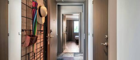 A hallway with a wooden floor, a patterned rug, and a wall-mounted rack holding hats and bags.