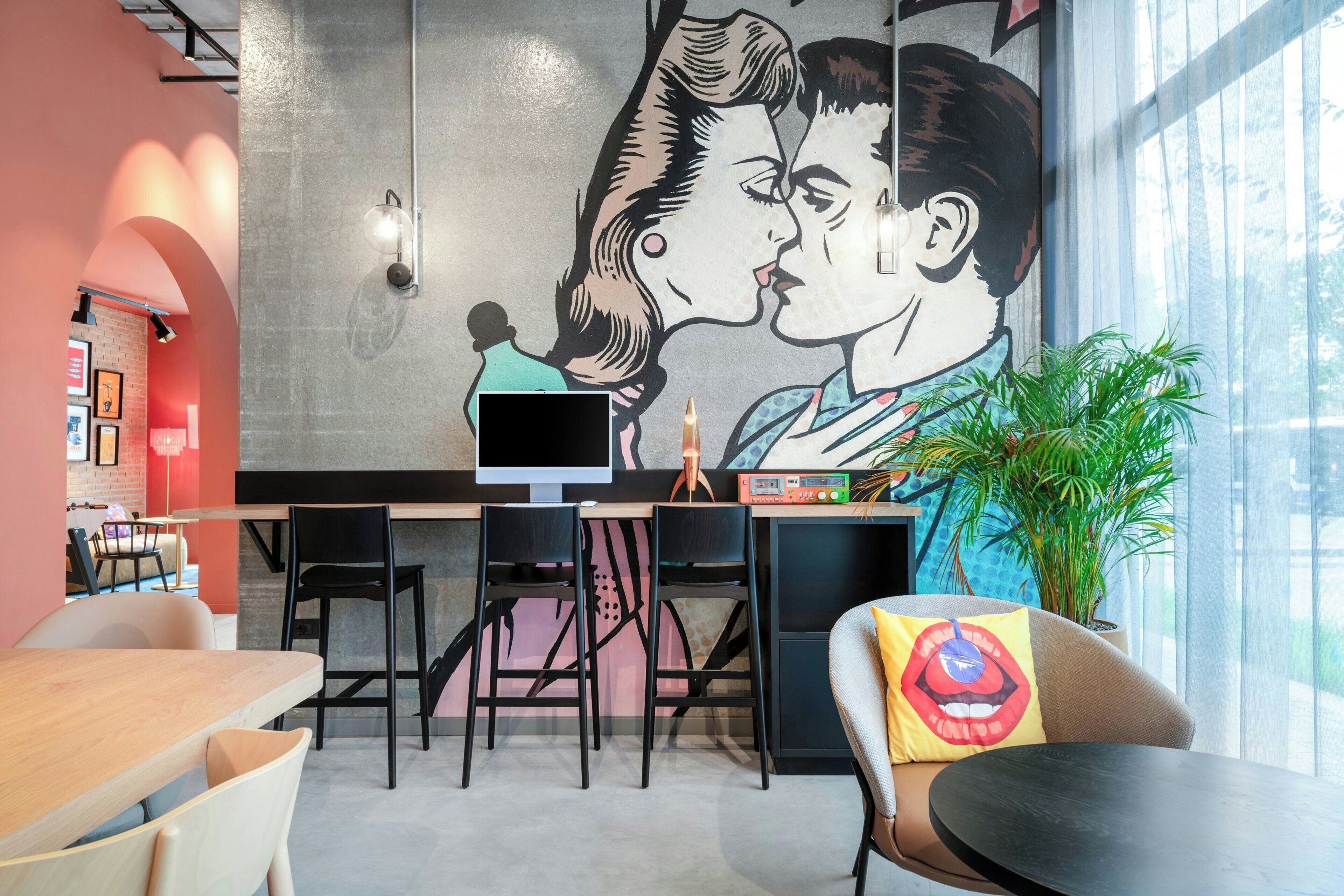 A modern cafe with a large mural of a couple kissing, a flat-screen TV, and a plant.