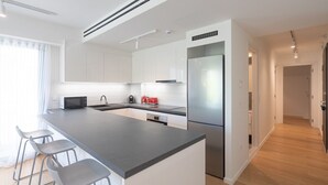 A modern kitchen with white cabinets, a stainless steel refrigerator, and a grey countertop.