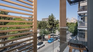 A balcony with wooden slats, a view of a street with parked cars, and a building with balconies in the background.