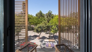 A view from a window with vertical blinds, overlooking a parking area with a white van and trees.