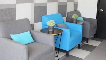 Un vestíbulo de hotel con una pared estampada de cuadros, dos sillones grises, un sofá azul y una pequeña mesa con una planta.