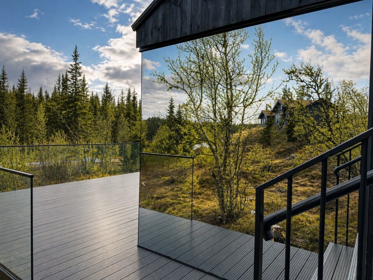 A modern outdoor deck with a glass railing, overlooking a forested area and a residential building.