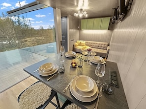 A modern dining area with a glass table, metal plates, and candles.