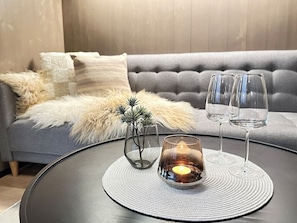 Una mesa redonda con un candelabro de cristal, dos copas de vino y una pequeña planta en maceta.