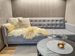 A grey sofa with a fluffy throw blanket, two wine glasses, and a candle on a round table.
