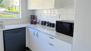Une cuisine moderne avec des meubles blancs, un lave-vaisselle noir, une machine à café et un four à micro-ondes.