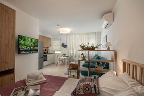 Una habitación de hotel moderna con cama, televisor, escritorio, silla y zona de cocina.