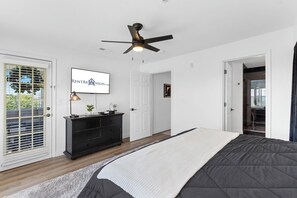 Ein Schlafzimmer mit Bett, Deckenventilator, Kommode, Fernseher und einer Tür mit Fenster.
