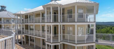 A multi-story building with balconies, a covered patio, and a view of the surrounding landscape.