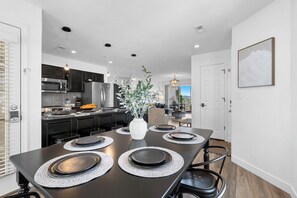Une cuisine moderne avec des meubles de couleur sombre, des appareils en acier inoxydable et un coin repas avec une table noire, mise pour quatre personnes.