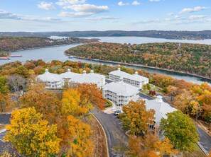 A large building with multiple wings, surrounded by autumn foliage and a body of water.