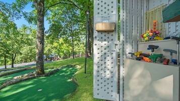 A playground with a climbing structure, a basketball hoop, and a green lawn.