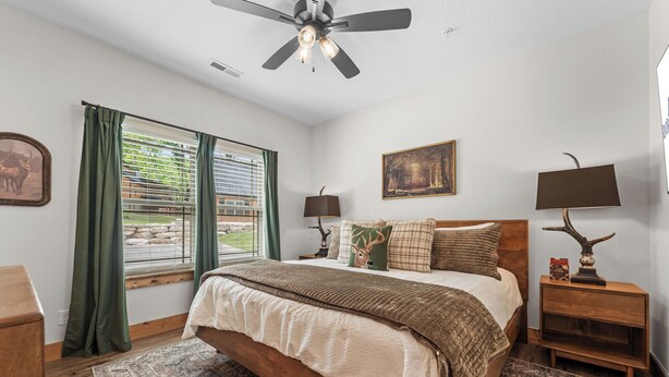 A bedroom with a bed, a ceiling fan, a nightstand, a lamp, and a window with curtains. - Private Hot Tub Cabin Near Table Rock with Free Tickets & Indoor/Outdoor Community Pools (Hollister)