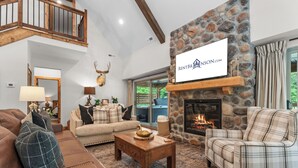 A spacious living room with a stone fireplace, a high ceiling, and a view of the outdoors. - Private Hot Tub Cabin Near Table Rock with Free Tickets & Indoor/Outdoor Community Pools (Hollister)