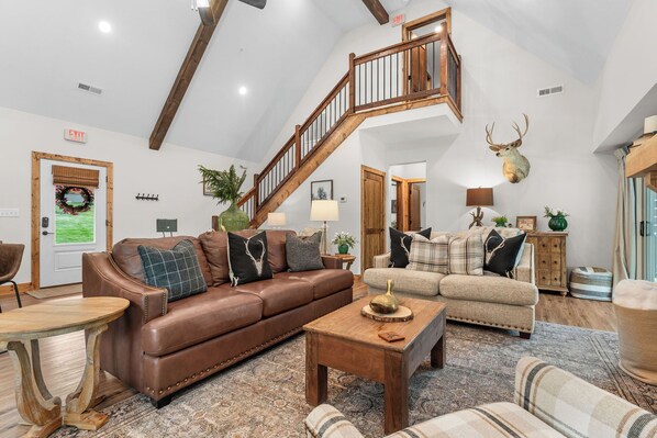 A spacious living room with a brown leather sofa, a beige sofa, a wooden coffee table, and a staircase with wooden railings.