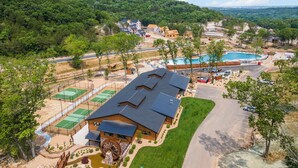 A residential area with multiple houses, a swimming pool, tennis courts, and a large wooden wheel structure. - Private Hot Tub Cabin Near Table Rock with Free Tickets & Indoor/Outdoor Community Pools (Hollister)