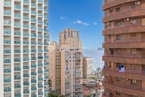 A high-rise building with multiple balconies, a view of the sea, and a neighboring building with a similar architectural style.