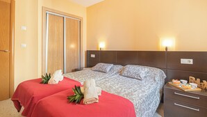 A hotel room with two beds, a wooden wardrobe, a nightstand with a tray of pastries, and a wall-mounted light fixture. - Benidorm Levante Beach 9A, Benidorm, Spain (Benidorm)