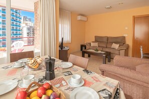 A furnished living room with a sofa, a dining table set with plates, cups, and a basket of fruit. - Benidorm Levante Beach 8B, Benidorm, Spain (Benidorm)