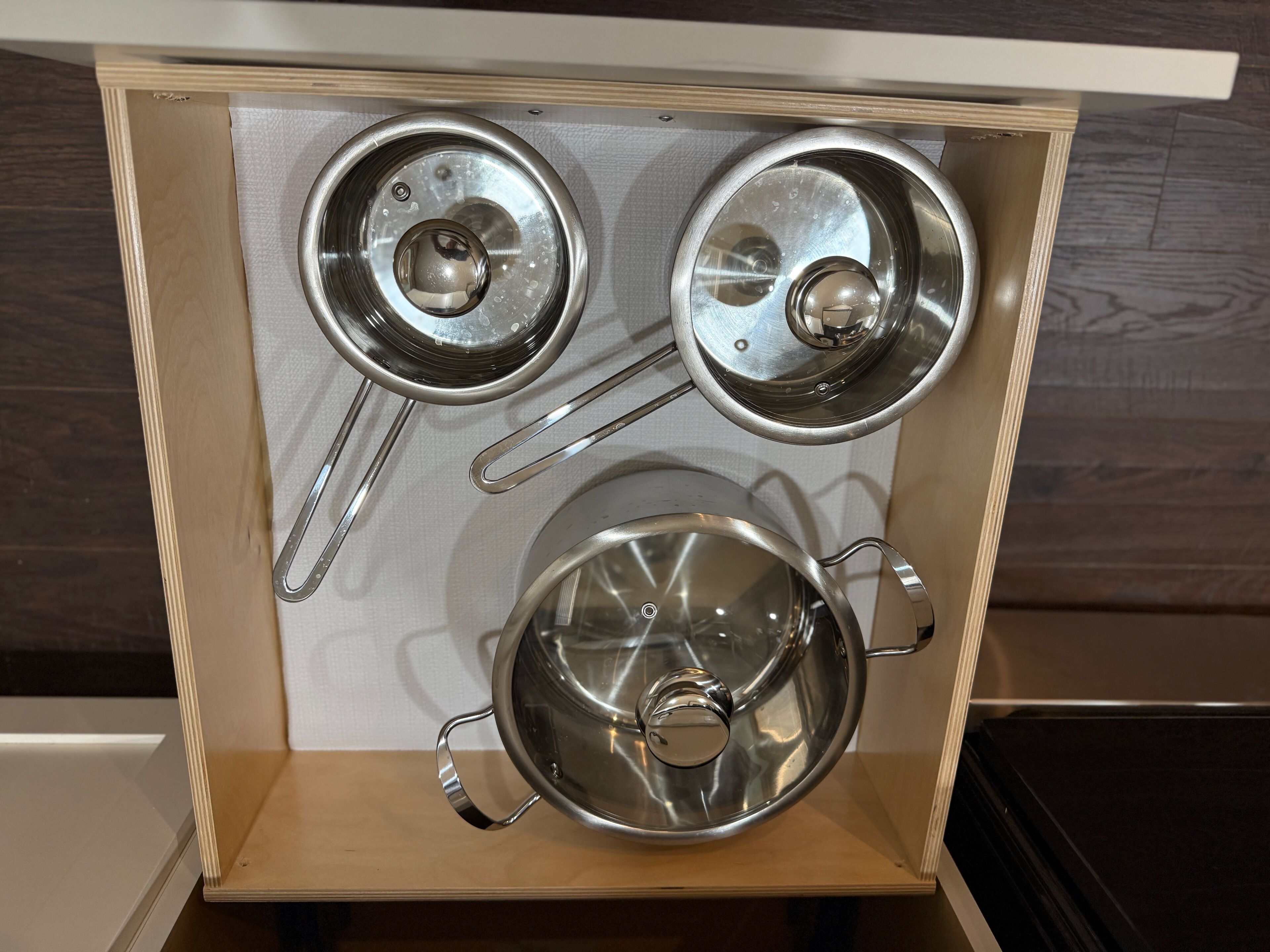 Un armario de cocina con utensilios de acero inoxidable, incluyendo una olla, dos tapas y una sartén.