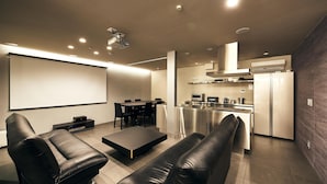 A modern living room with a flat-screen TV, leather sofas, a coffee table, and a dining area with chairs and a table. - MUSASHI Condo Shinjuku (Tokyo)