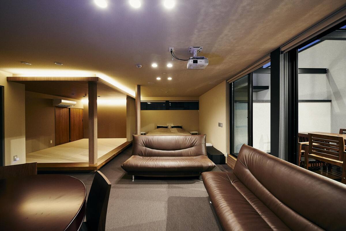 A modern, well-lit room with a large bed, a sofa, and a dining area.