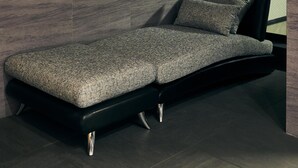 A modern room with a minimalist design, featuring a dark-toned sofa against a textured wall, a large window providing natural light, and a sleek, dark floor. - MUSASHI Condo Shinjuku (Tokyo)