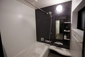 A modern bathroom with a bathtub, a shower, a large mirror, and a dark textured wall. - MUSASHI Condo Shinjuku (Tokyo)