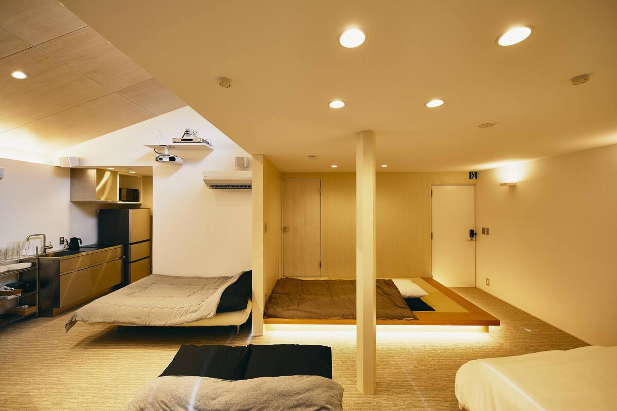 A modern hotel room with a kitchenette, two beds, and a large window.