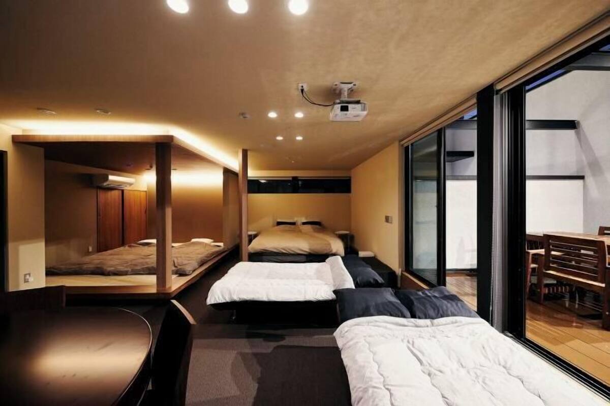 A compact hotel room with three beds arranged in a row, a ceiling projector, and a large sliding glass door leading to an outdoor area.