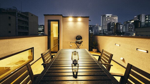 A rooftop terrace with a dining table and chairs, a lantern, and a small grill. - MUSASHI Condo Shinjuku (Tokyo)