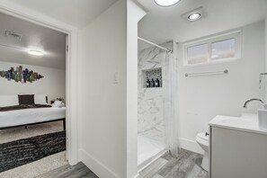 Una camera da letto moderna con un letto, un elemento decorativo a parete e un tappeto bianco e nero. Il bagno è dotato di una vasca, un water e un lavandino con specchio sopra.