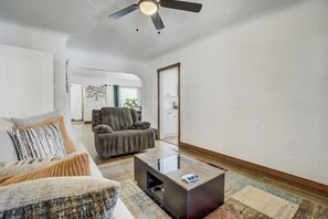 Un soggiorno con divano, poltrona, tavolino e ventilatore a soffitto.