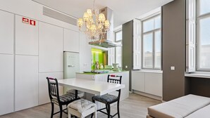 A modern kitchen with a white countertop, a chandelier, and a dining area with a table and chairs. - GuestReady - AMMA Braga - 10 (Braga)