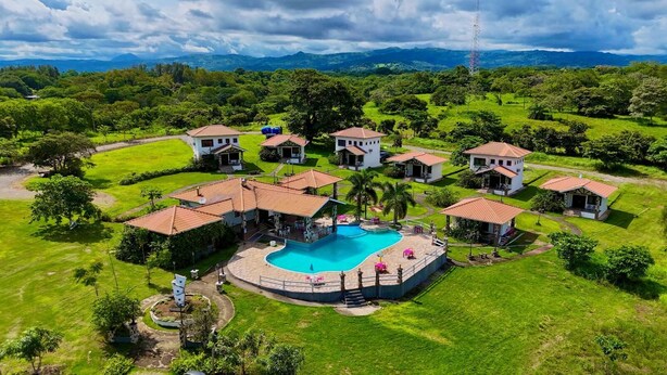 An aerial view of a resort with a central swimming pool, multiple villas with red-tiled roofs, and lush green surroundings. - Country Hills Las Lajas (San Felix)