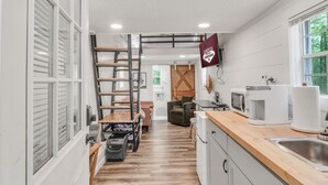 A compact kitchen with a wooden countertop, a sink, and a microwave. There is a small dining area with a table and chairs.
