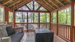 A covered porch with a wooden bench, two chairs, and a table.