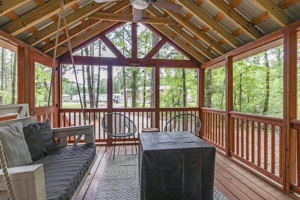 A covered porch with a wooden bench, two chairs, and a table. - OutBack, Glamping, Screened-In Sunsets (Starkville)