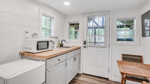 A compact kitchen with white cabinetry, a microwave, a coffee maker, and a small refrigerator. There is a wooden countertop and a dining table with chairs.