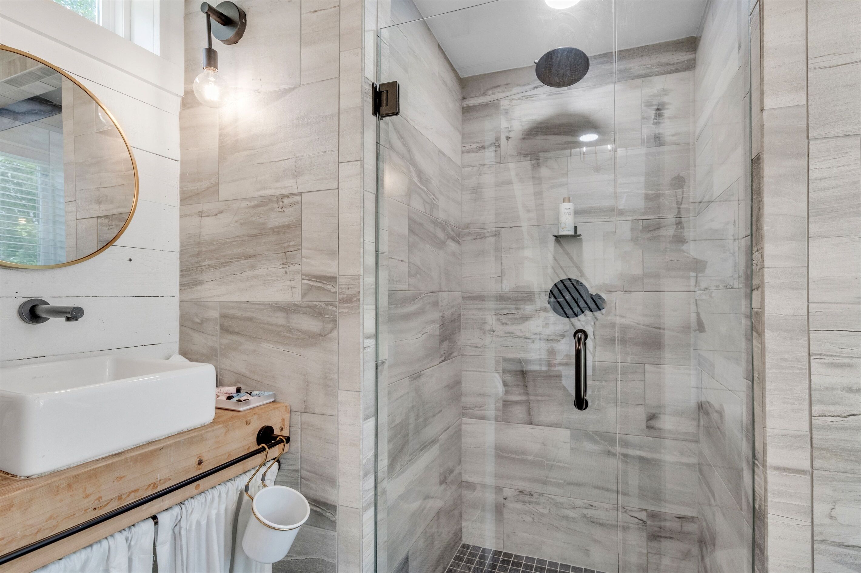 A modern bathroom with a white sink, wooden countertop, and a glass shower enclosure.