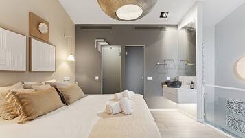 A modern bedroom with a large bed, a bedside table, a mirror, and a bathroom with a sink and shower.