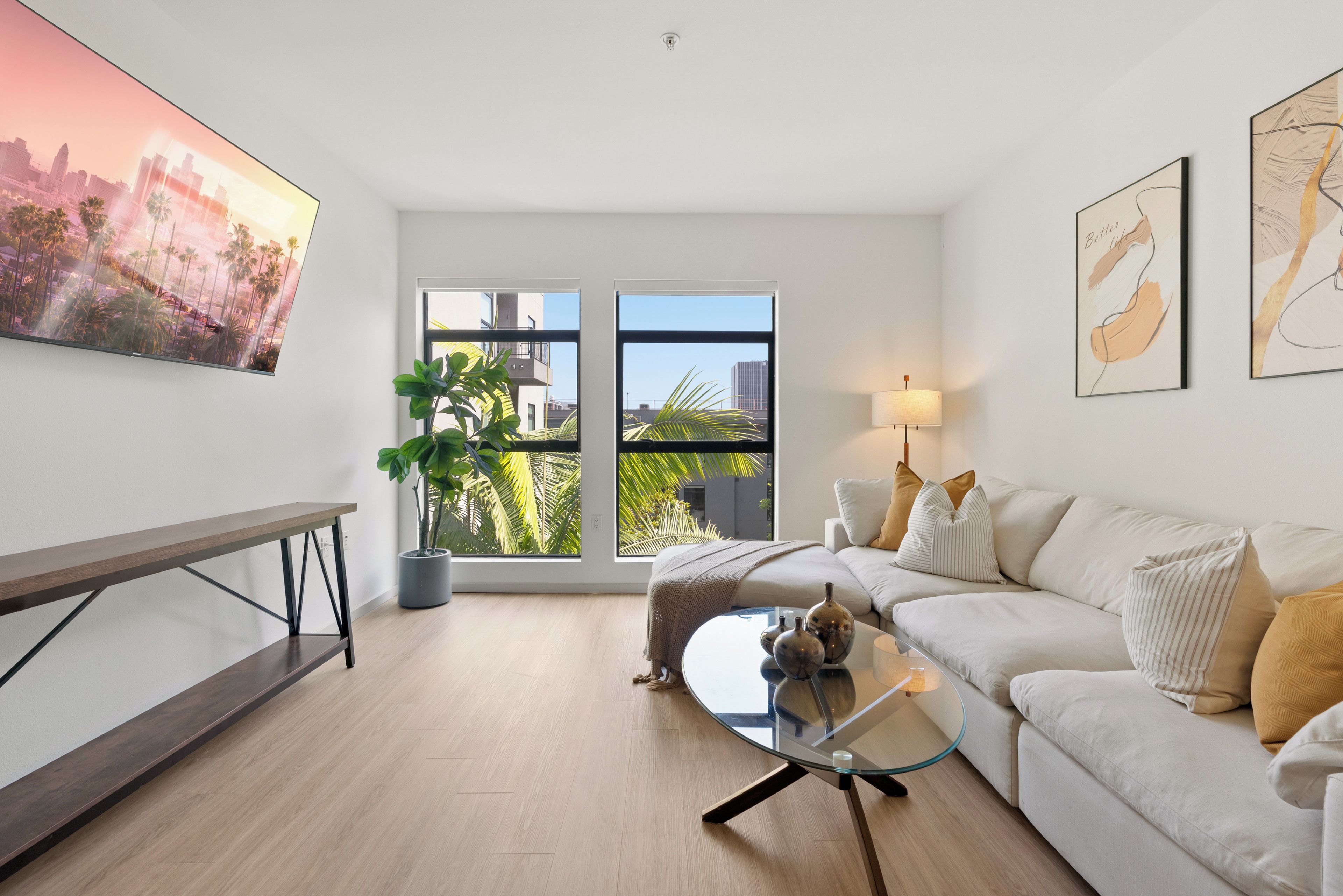A modern living room with a glass coffee table, a sofa, a bench, and a large window offering a city view.