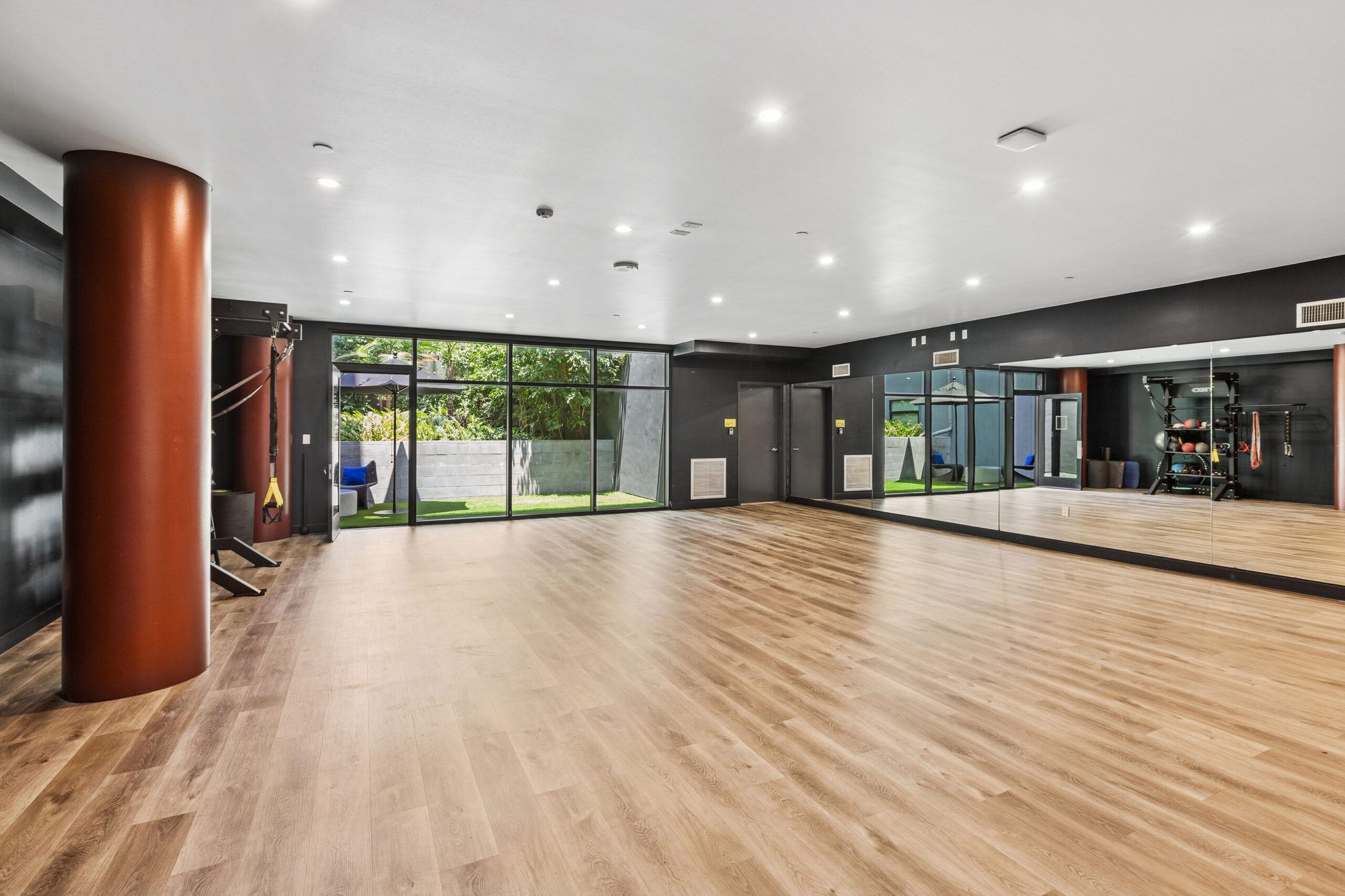 A spacious gym with wooden flooring, large windows, and exercise equipment.